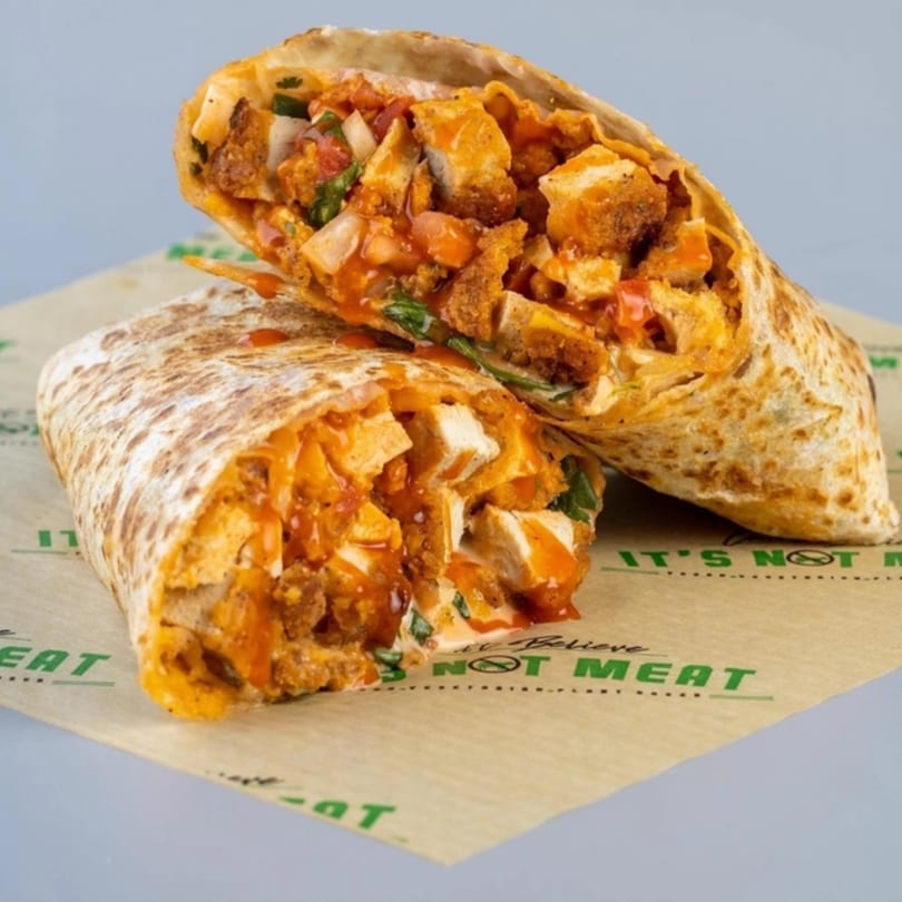 Two halves of a vegan buffalo chicken wrap, filled with plant-based chicken, sauce, and vegetables.