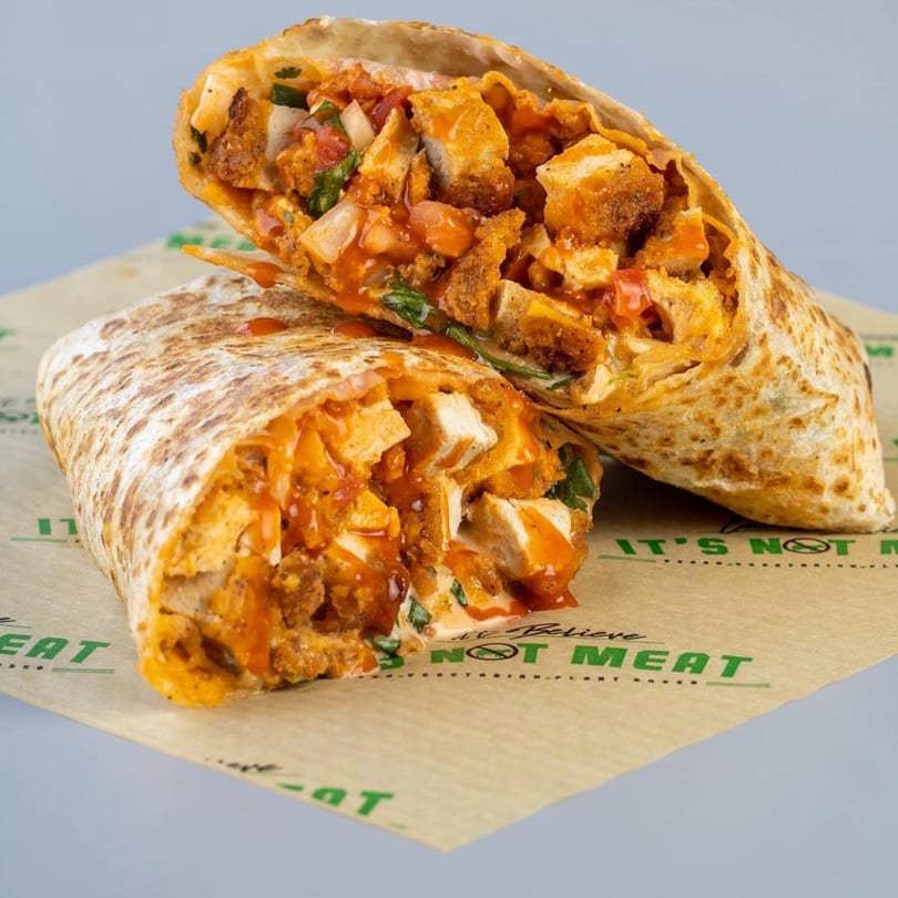 Two halves of a vegan buffalo chicken burrito, filled with plant-based chicken, sauce, and vegetables.