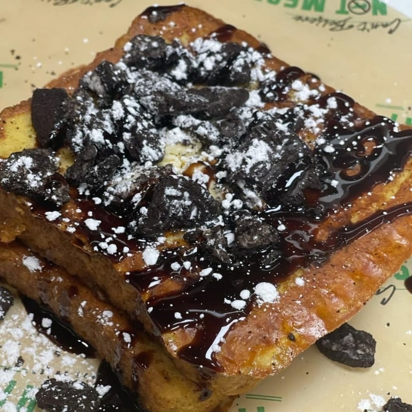 Thick-cut vegan French toast topped with chocolate syrup, crushed cookies, and powdered sugar.
