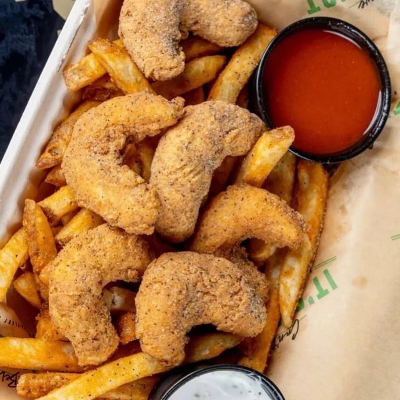 Vegan fried shrimp and french fries with red and white dipping sauces in a paper container.