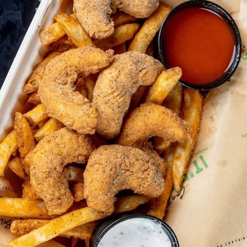 Vegan fried shrimp and french fries with red and white dipping sauces in a paper container.
