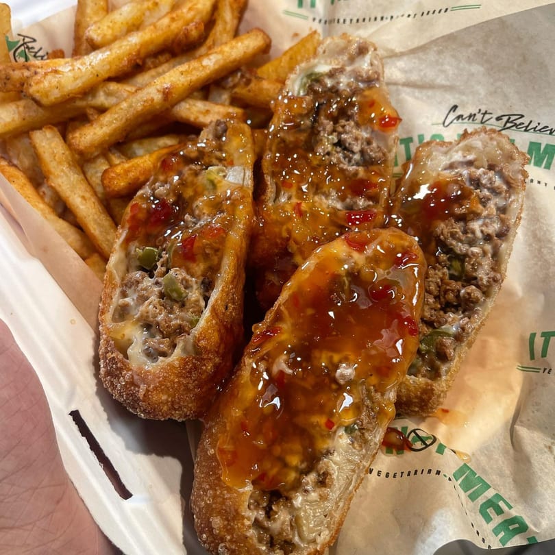 Vegan egg rolls with sweet chili sauce and a side of french fries in a paper-lined basket.