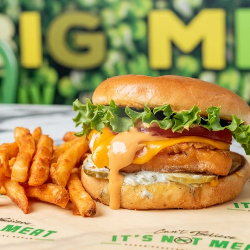 Vegan burger with melted cheese, special sauce, lettuce, tomato, pickles, and a side of fries.